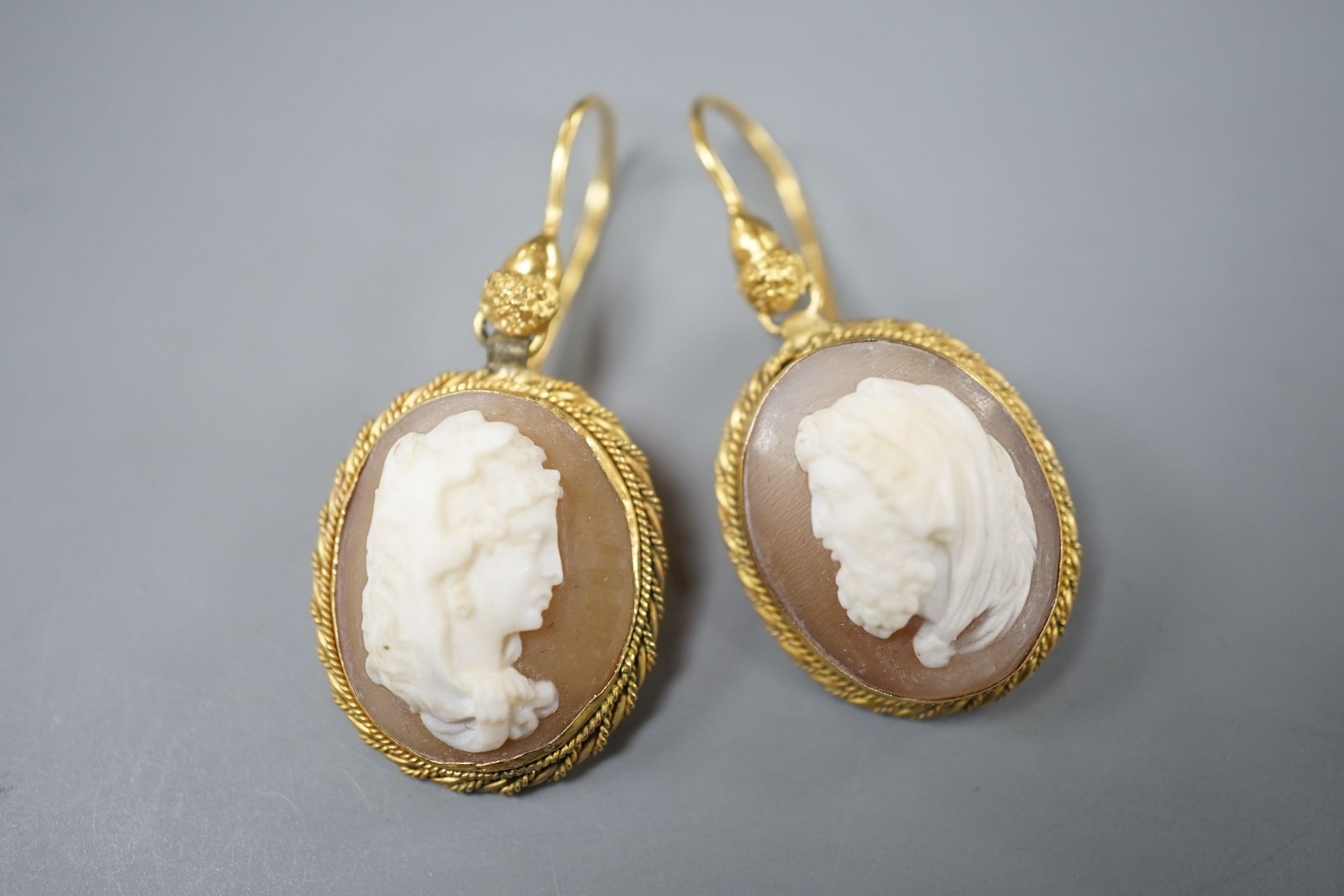 A pair of early 20th century yellow metal and oval cameo shell earrings, carved with a lady to sinister and a gentleman to dexter, overall 40mm, gross 6.2 grams.